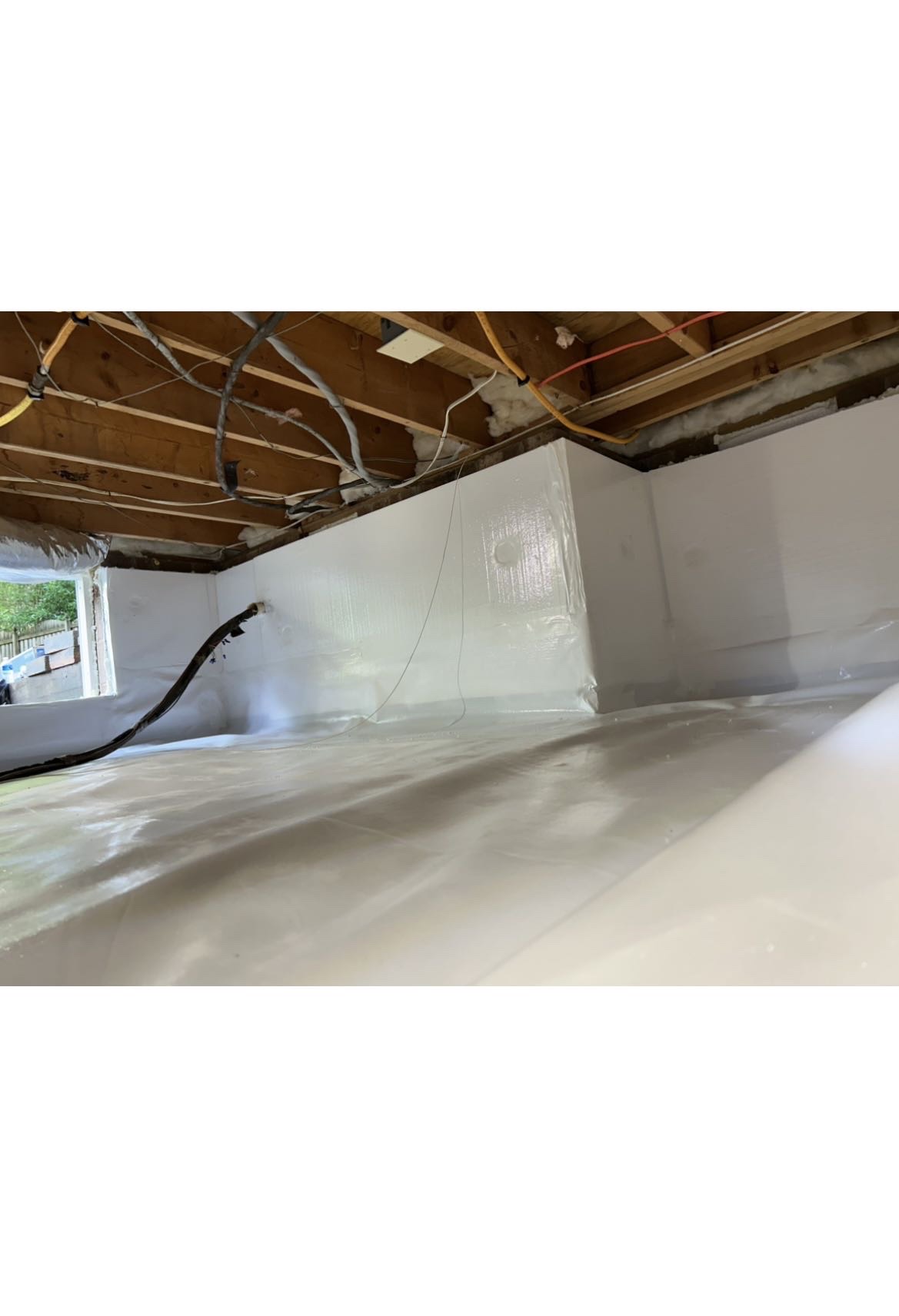Crawlspace encapsulation showing white vapor barrier installation with dehumidifier hose running overhead