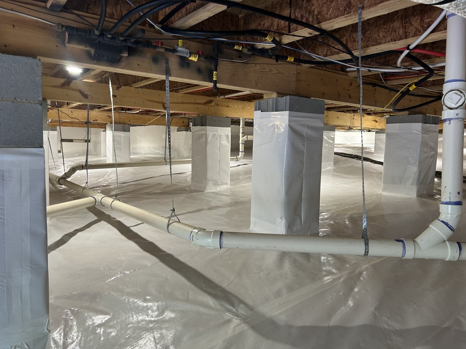 Wide view of a completed crawlspace encapsulation with sealed white vapor barrier and wrapped support piers